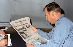Mężczyzna czyta gazetę z nagłówkiem o sukcesie astronautów, siedząc przy stole.